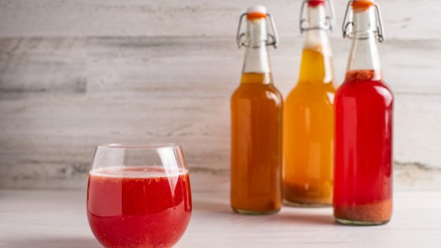 Fermented strawberry kombucha tea with plain, pineapple and strawberry bottles in the background.