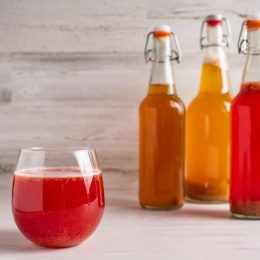 Fermented strawberry kombucha tea with plain, pineapple and strawberry bottles in the background.