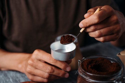 man fills the funnel of a moka pot with ground coffee, sitting at a gray rustic wooden table
