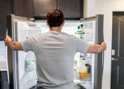 A man looking into his open freezer and refrigerator