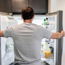 A man looking into his open freezer and refrigerator