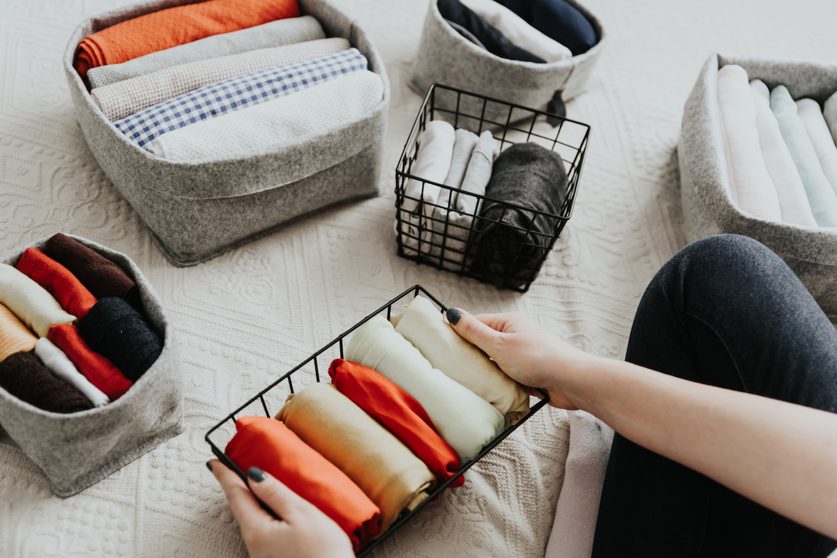 Close up of a woman organizing clothes into bins on her bed.