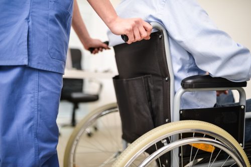 O asistentă are grijă de un pacient într-un scaun cu rotile