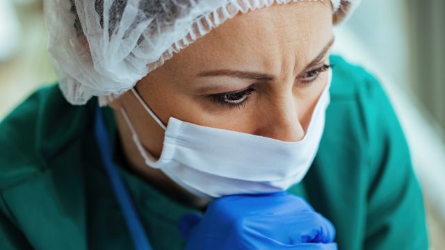 Close-up of pensive female doctor wearing protective workwear and thinking of something while working at medical clinic.