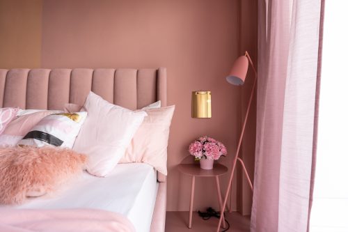 Cozy Pink Bedroom corner with baby pink velvet fabric bed decorated by blanket, pillows and pink floor lamp with two-tone pink painted wall on the background