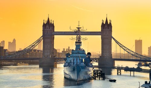 HMS Belfast moored in front of Tower Bridge on the River Thames at sunrise.