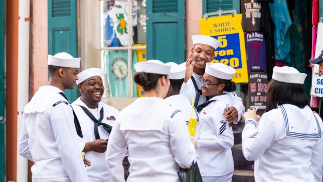 Old town street in Louisiana city with happy people sailors group holding drinks talking on sidewalk during Navy Week.