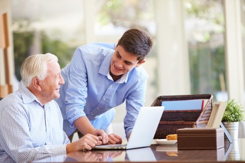 Young man helping senior man on computer
