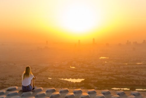 Woman sitting on top of skyscraper overlooking the city at sunrise.