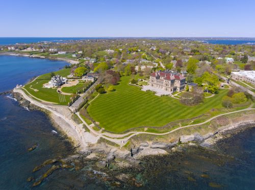 An aerial view of the Italian Renaissance-style mansion The Breakers in Newport, Rhode Island, with the ocean and cliff walk surrounding it.