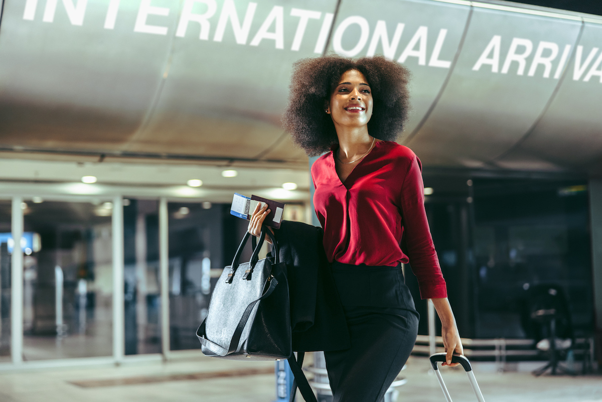 A smiling woman walking with her suitcase in the international arrivals terminal at an airport.