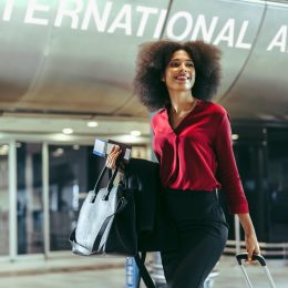 A smiling woman walking with her suitcase in the international arrivals terminal at an airport.