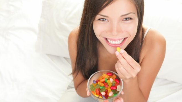 Candy woman eating sweets with a fresh smile in bed.
