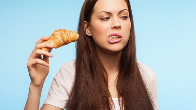 Woman eating croissant with open mouth.