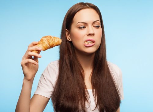 Người phụ nữ ăn bánh sừng bò với miệng mở.