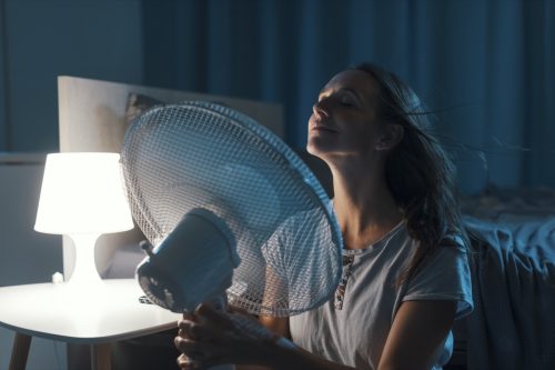 Woman in her bedroom on a hot summer night, she is enjoying fresh air in front of a fan
