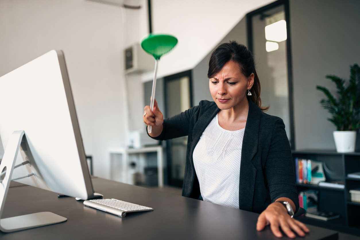 A woman in a suit sitting at a desk using a flyswatter to kill an insect