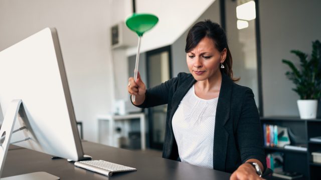 A woman in a suit sitting at a desk using a flyswatter to kill an insect