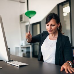 A woman in a suit sitting at a desk using a flyswatter to kill an insect