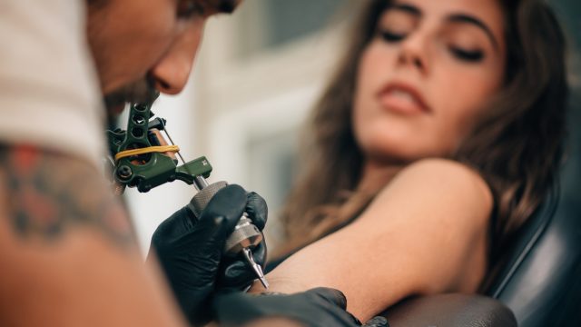 A young woman getting a tattoo on her harm