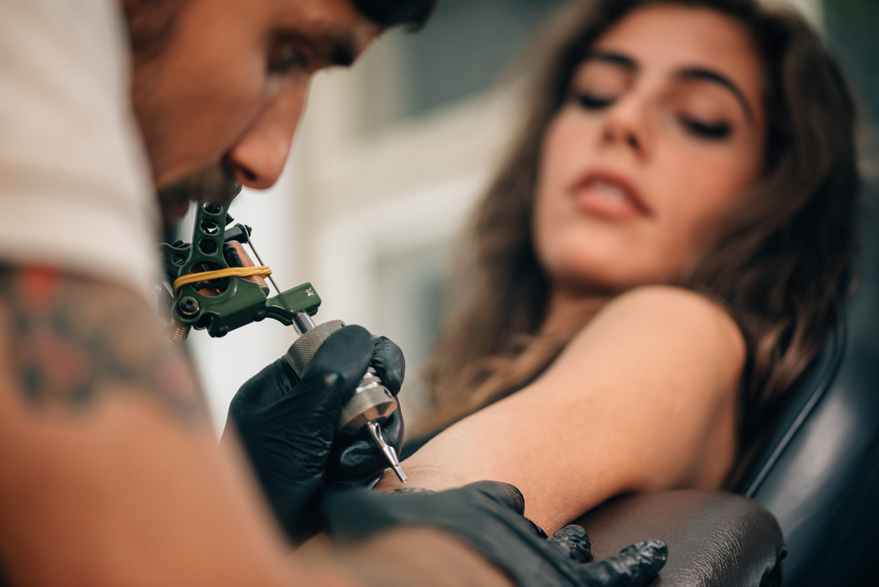 A young woman getting a tattoo on her harm