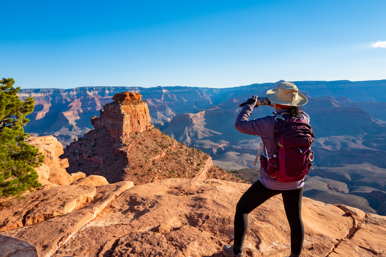 Một người phụ nữ đứng bên rìa Grand Canyon chụp ảnh