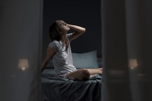 Tired woman sitting in bed at night with open window