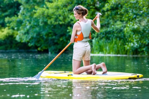 Woman paddling with surfboard sup on forest river