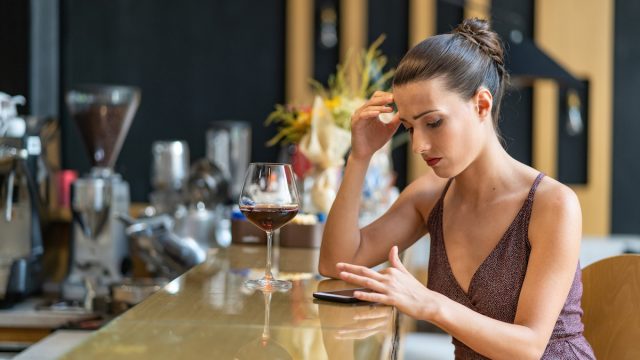 Sad woman sitting at a bar being stood up and using smart phone