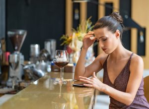 Sad woman sitting at a bar being stood up and using smart phone