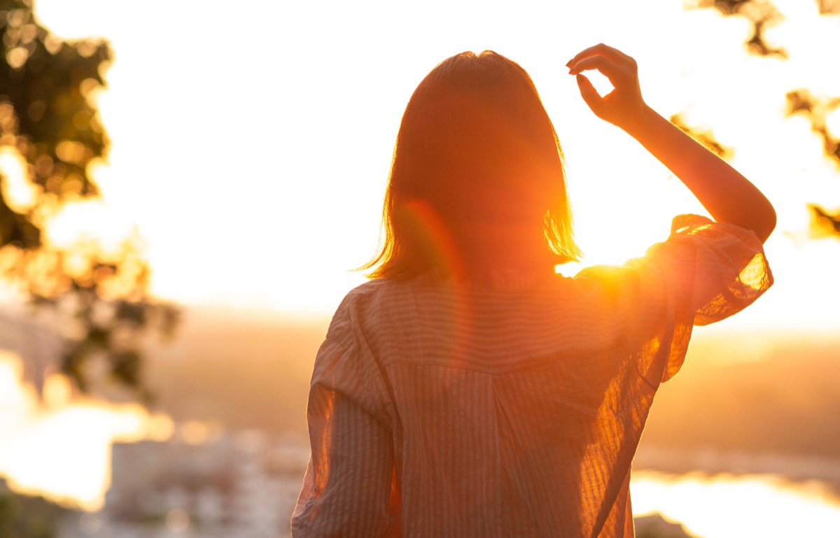 Young woman in casual shirt looking at sunset at the park.