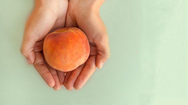 Ripe juicy peach in the woman's hands on the grey table.