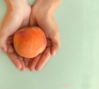 Ripe juicy peach in the woman's hands on the grey table.