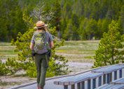 Outdoor view of female park ranger wearing a green uniform with a backpack, walking along the wooden path in the Old Faithful Upper Geyser Basin