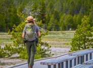 Outdoor view of female park ranger wearing a green uniform with a backpack, walking along the wooden path in the Old Faithful Upper Geyser Basin