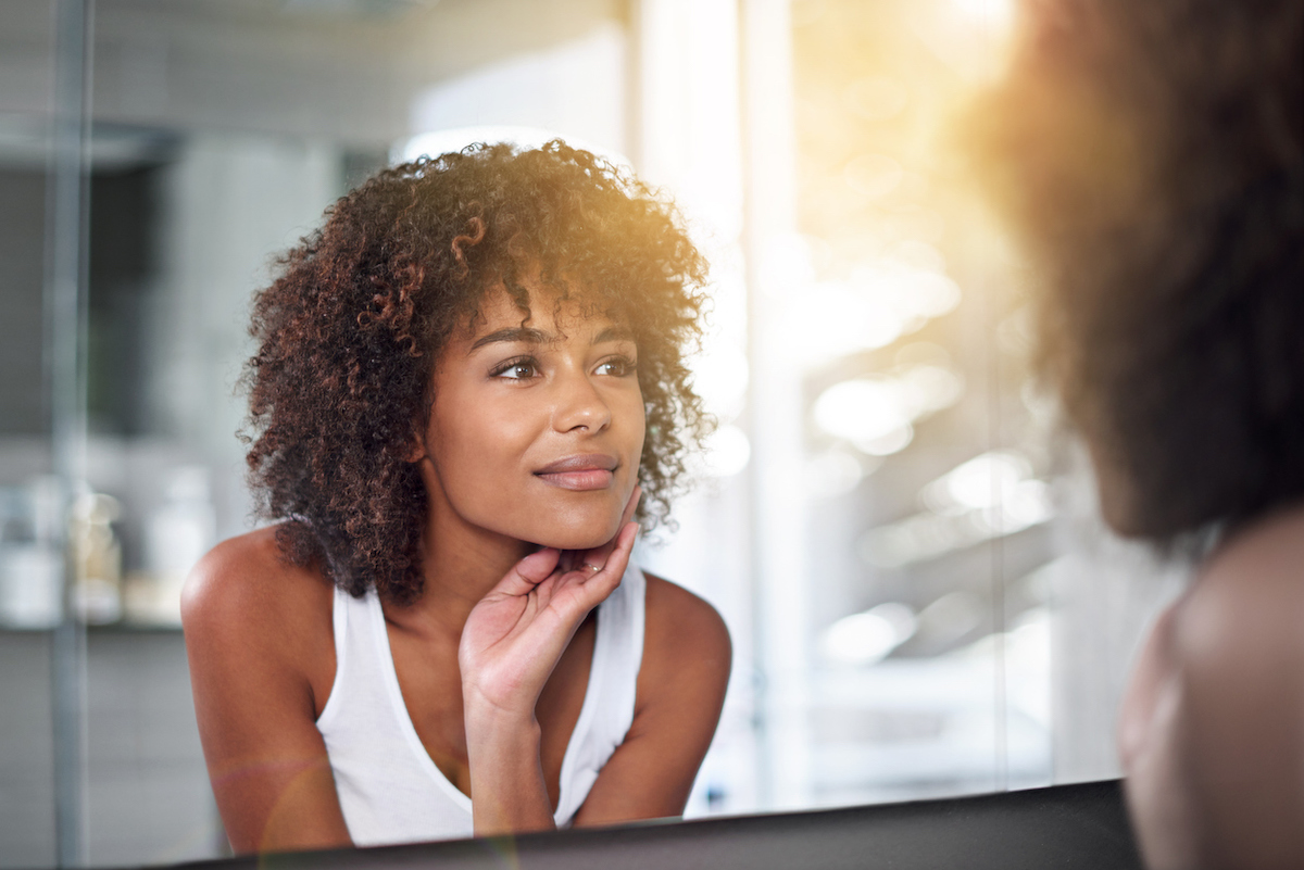 Cropped shot of a young woman examining her skin in the bathroom mirror.