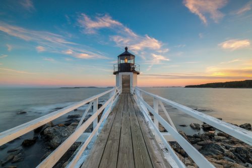 Maine's Marshall Point lighthouse at sunset, with the dock leading up to it.