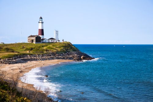 The red and white Montauk Point Lighthouse with the shore and ocean in the foreground.