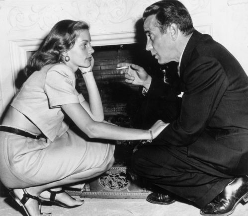 Lauren Bacall and Humphrey Bogart kneeling in front of a fireplace in their home circa 1945