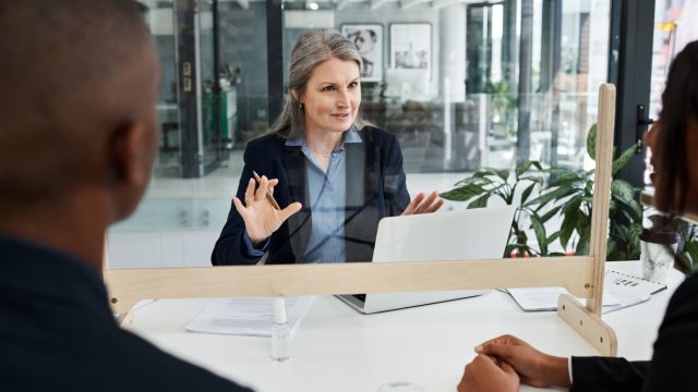 Shot of a mature businesswoman having a meeting with a sneeze guard in a modern office