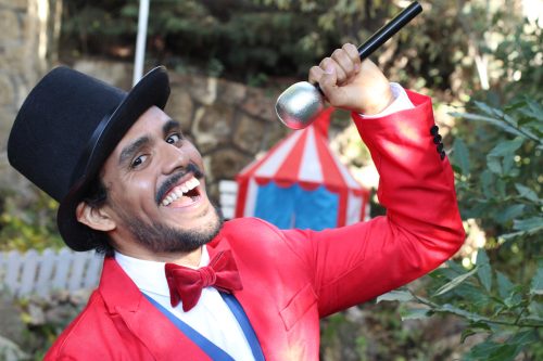 A young man dressed up as a circus ringmaster with a microphone