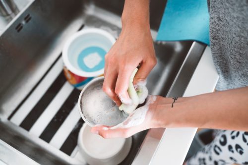 Unrecognizable woman hands washing dog bowl in the kitchen sink.