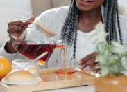 Cropped image of young Black woman making herself a cup of tea with croissants for breakfast