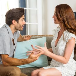Young couple arguing on the couch in a bright, sunny living room.