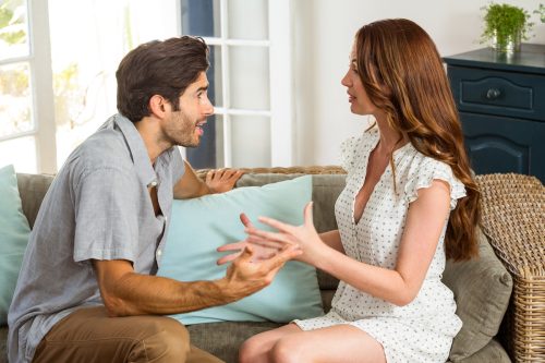 Young couple arguing on the couch in a bright, sunny living room.
