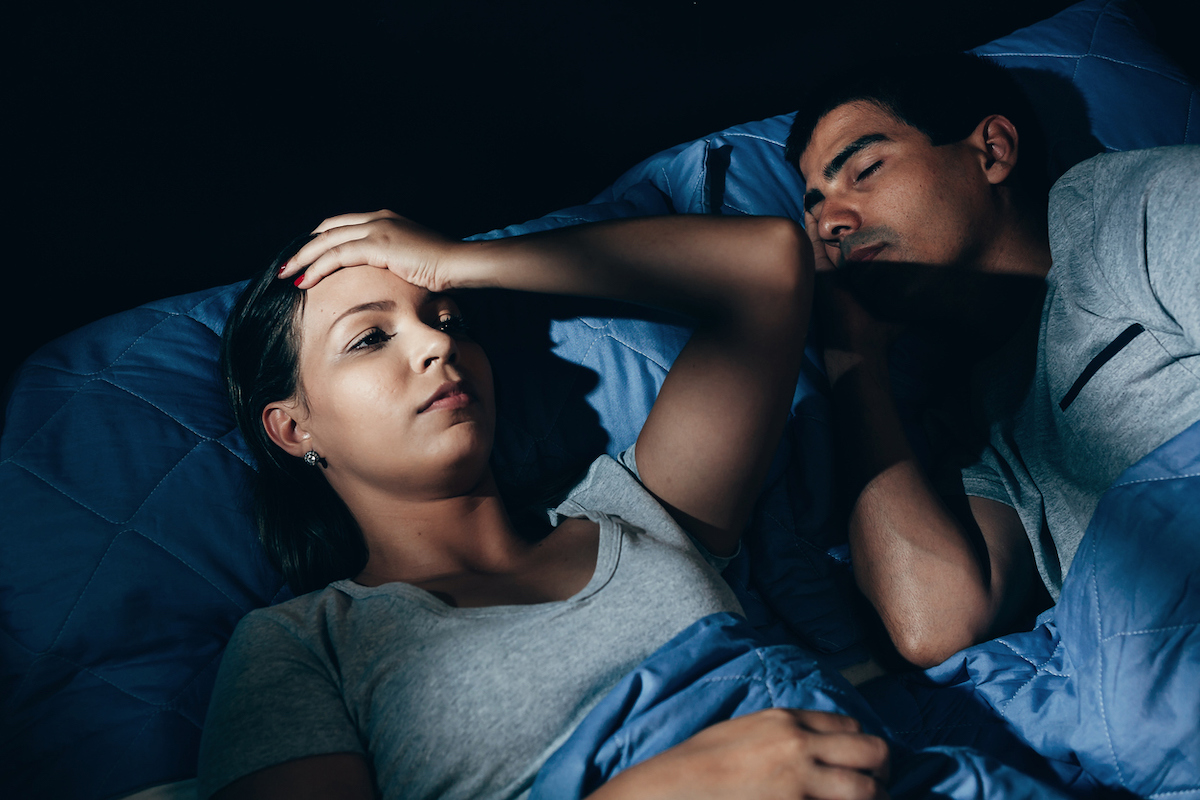 Annoyed woman lying awake in bed with snoring boyfriend at home in the bedroom