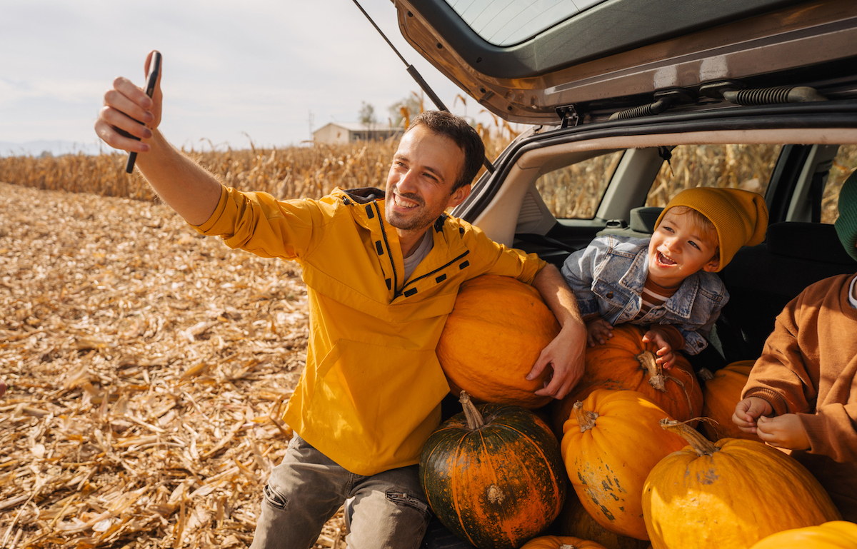 Photo of a young father and his sons taking pictures in a car trunk full of pumpkins