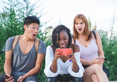 three friends looking at truth or dare questions on their phone and appearing shocked