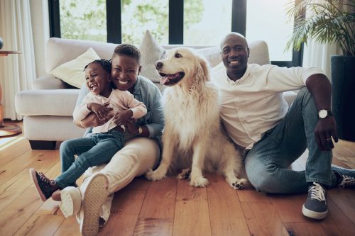 Shot of a young couple sitting on the living room floor with their daughter and big white dog.