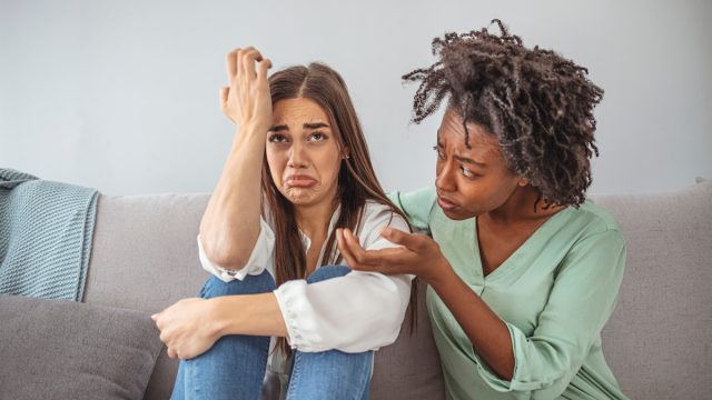 Young lady sharing her problem with friend. female in depression. Woman omforting hes sad friend sitting on a couch in the living room at home